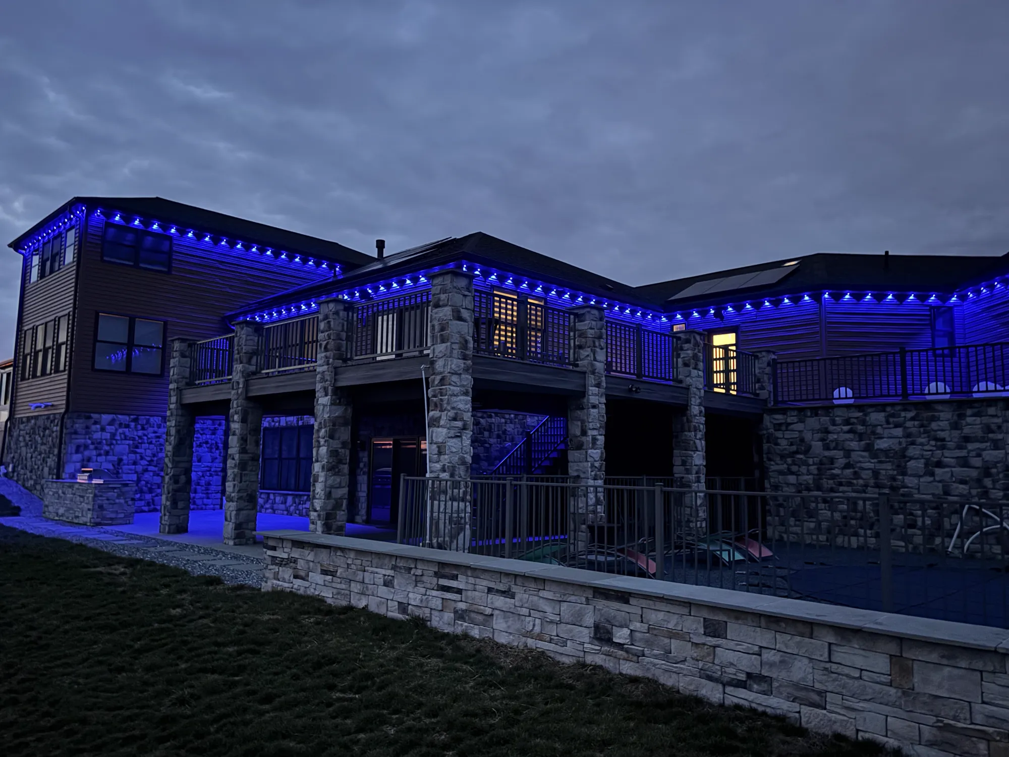 Large stone-and-siding home with Govee permanent lights glowing blue along every roofline at dusk