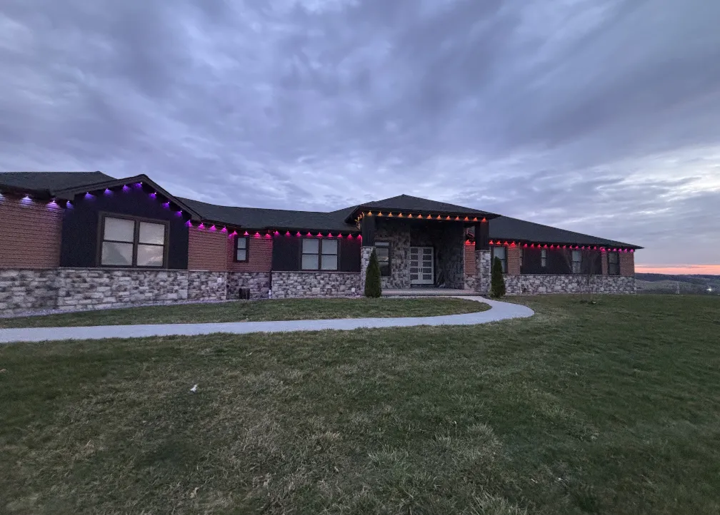 Wide view of a stone ranch home with purple and red permanent lighting across the full roofline